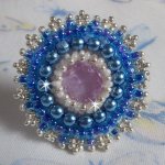 Bague Azur brodée avec un cabochon en Cristal de couleur Antique Pink à laquelle s'ajoute des rocailles et perles rondes nacrées. Le tout est monté sur une bague filigranée Blanche